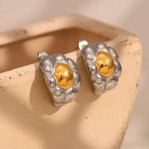 Detail showing two-tone 18K gold plated horn stud earrings on a beige pottery vase