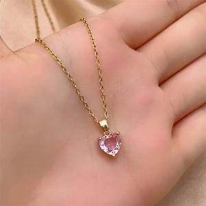 Detailed macro view of a gold heart necklace with a pink zircon gemstone held in hand