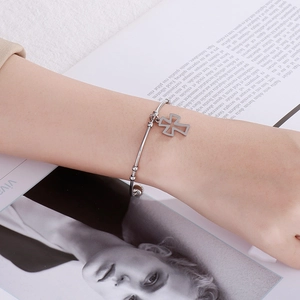 Silver stainless steel cross charm bracelet worn by a model against a magazine backdrop
