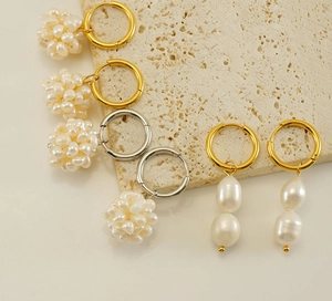 Détail de boucles d'oreilles créoles dorées 18k et argentées avec perles sur pierre beige