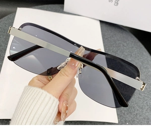 Detail showing hand holding rimless rectangular sunglasses with gradient gray lenses