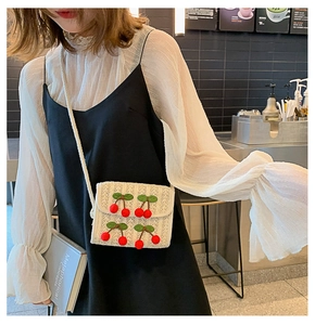 Detail of a white woven crossbody bag featuring decorative 3D red plush cherries