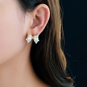 Boucles d'oreilles nœud plaquées or 14K avec émail blanc sur un mannequin femme