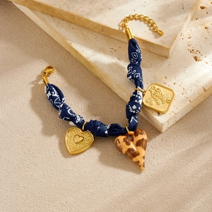Blumiges Stoffarmband mit goldenem Herz und Rosenanhängern auf Steinuntergrund