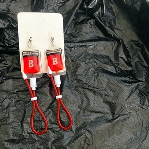 Detailed close-up of a Blood Group B drip bag earring on a black textured background