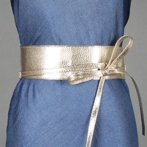 Detail eines breiten goldenen Obi-Gürtels mit Lychee-Struktur auf blauem Faltenkleid