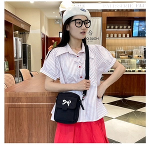 Detail of black bow-patterned canvas crossbody bag worn by model in a casual cafe setting