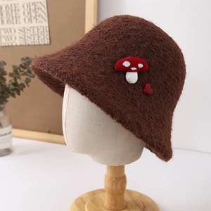 Detail of plush brown bucket hat featuring red mushroom and heart accents on a wooden model