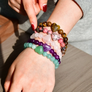 Close-up of stacked natural stone beaded bracelets with heart charms on a wrist