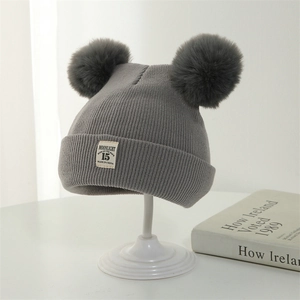 Close-up of gray knitted baby hat featuring dual pom-poms and a detailed fabric label