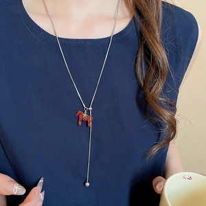 Detail of a silver snake chain Y-necklace with red pony pendant worn on a model