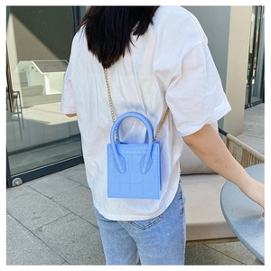 Macro shot of light blue croc-embossed mini bag with golden chain strap on a model