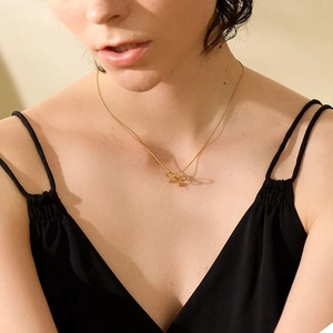 Dettaglio della collana dorata con ciondolo a fiocco e perline indossata da modella