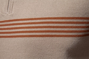 Macro shot of khaki knit polo shirt fabric featuring three parallel orange stripes