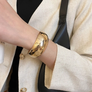 Bracelet jonc large doré poli au poignet du mannequin avec effet miroir brillant