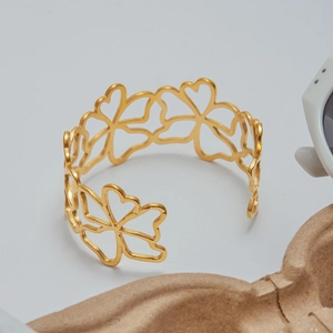 Detail of gold open bangle featuring hollow four-leaf clover and heart patterns