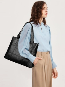 Detail of a black quilted tote bag with square panels and long shoulder straps