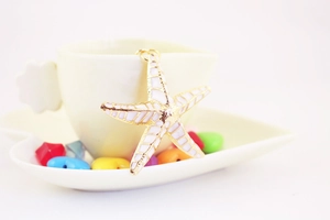 Close-up of white starfish keychain pendant hanging on a cream coffee cup with colorful beads