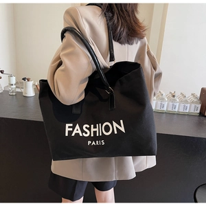 Bolso tote grande de lona negra con estampado FASHION PARIS llevado por modelo en café