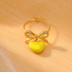 Detail of gold bow ring with yellow heart pendant on elegant gold silk fabric