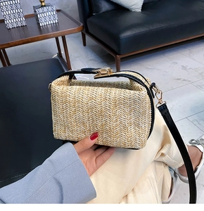 Close-up of woven straw handbag texture featuring black leather strap and gold metal clasp