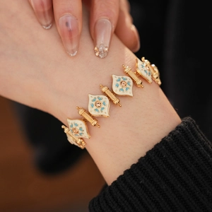 Macro shot of a vintage gold bracelet with white enamel, blue patterns, and orange crystals