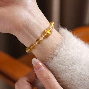 Detail of yellow citrine gourd flower bracelet worn on wrist with gold heart pendant