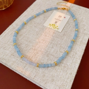 Macro detail of heart necklace with light blue stones and gold rings on linen texture
