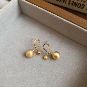 Detail of gold plated matte metal stud earrings with dual spheres and twisted geometric design