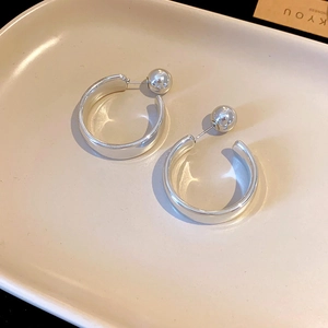 Detail of silver C-shaped hoop earrings with metal ball backs on a ceramic tray