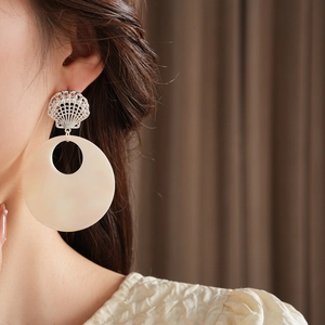 Close-up of a woman wearing large starfish shell stud earrings with cream hoop charms