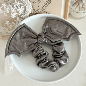 Detail of metallic grey bat wing bow hair scrunchie on a white ceramic display plate