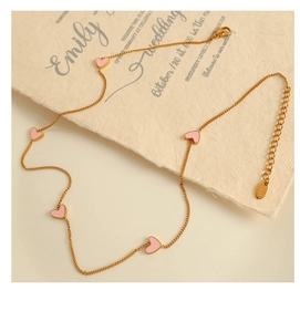 Detail of gold necklace with five pink enamel hearts on a delicate link chain