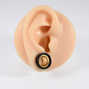 Close-up of black and gold two-tone hollow ear gauge plug on a realistic silicone ear model
