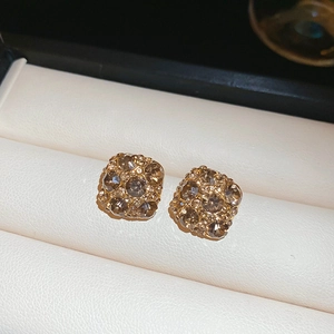 Close-up of gold plated square stud earrings with amber rhinestones in a luxury jewelry box