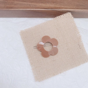 Detailed top view of a light brown resin flower hair clip on a soft beige linen fabric