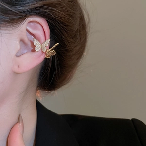 Detail of a golden double butterfly ear cuff with sparkling zircon on a female ear
