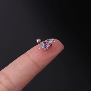 Macro view of heart-shaped arrow stud earring with pink zircon on fingertips