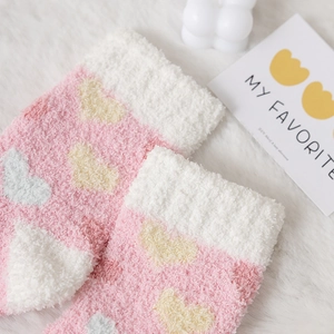 Pink and white coral fleece socks with heart patterns on a soft white plush rug