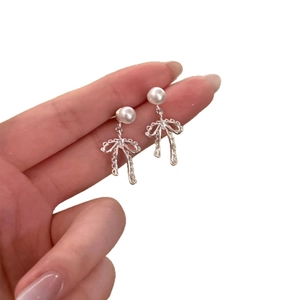 Elegant pearl bow drop earrings featuring silver needle studs and vintage textured ribbons