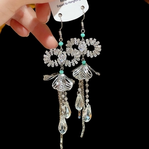 Detail of silver tassel earrings with zircon bow and turquoise beads on black background