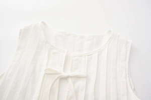 Detail of white pleated linen top featuring sleeveless design and tie neckline texture
