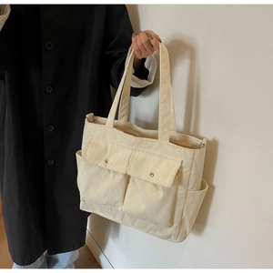Detail of off-white corduroy tote bag featuring multi-pocket design and metallic snap buttons