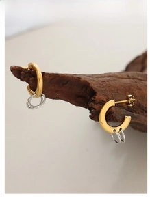 Detail of mixed-tone C-shaped gold earrings with interlocking silver rings on wood