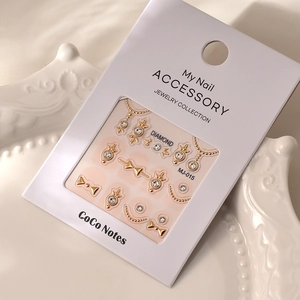 Detail of 3D gold bow and rhinestone crown nail art stickers on a vintage white plate