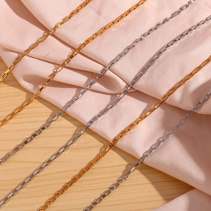 Close-up of gold and silver square box chains on pink silk and light wood background
