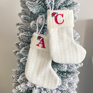 Detail of white knit Christmas stockings with red embroidered letters A and C on a tree