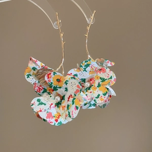 Close-up of golden branch earrings with colorful floral tassels and pearl accents
