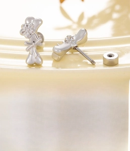 Detailed view of silver bone-shaped stud earring with cubic zirconia bow and flower accents