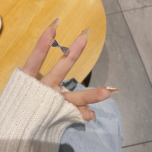 Close-up of a silver bow knot ring on a finger, showing a delicate twisted cross design